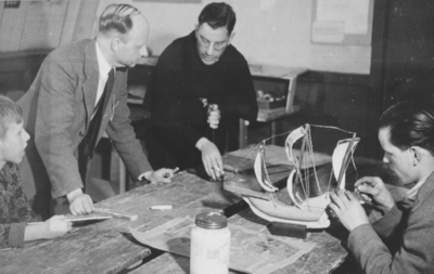 876589 Portret van een jongen, lid van een 'huisvlijtclub' van het St. Franciscus Liefdewerk, die een modelbootje aan ...